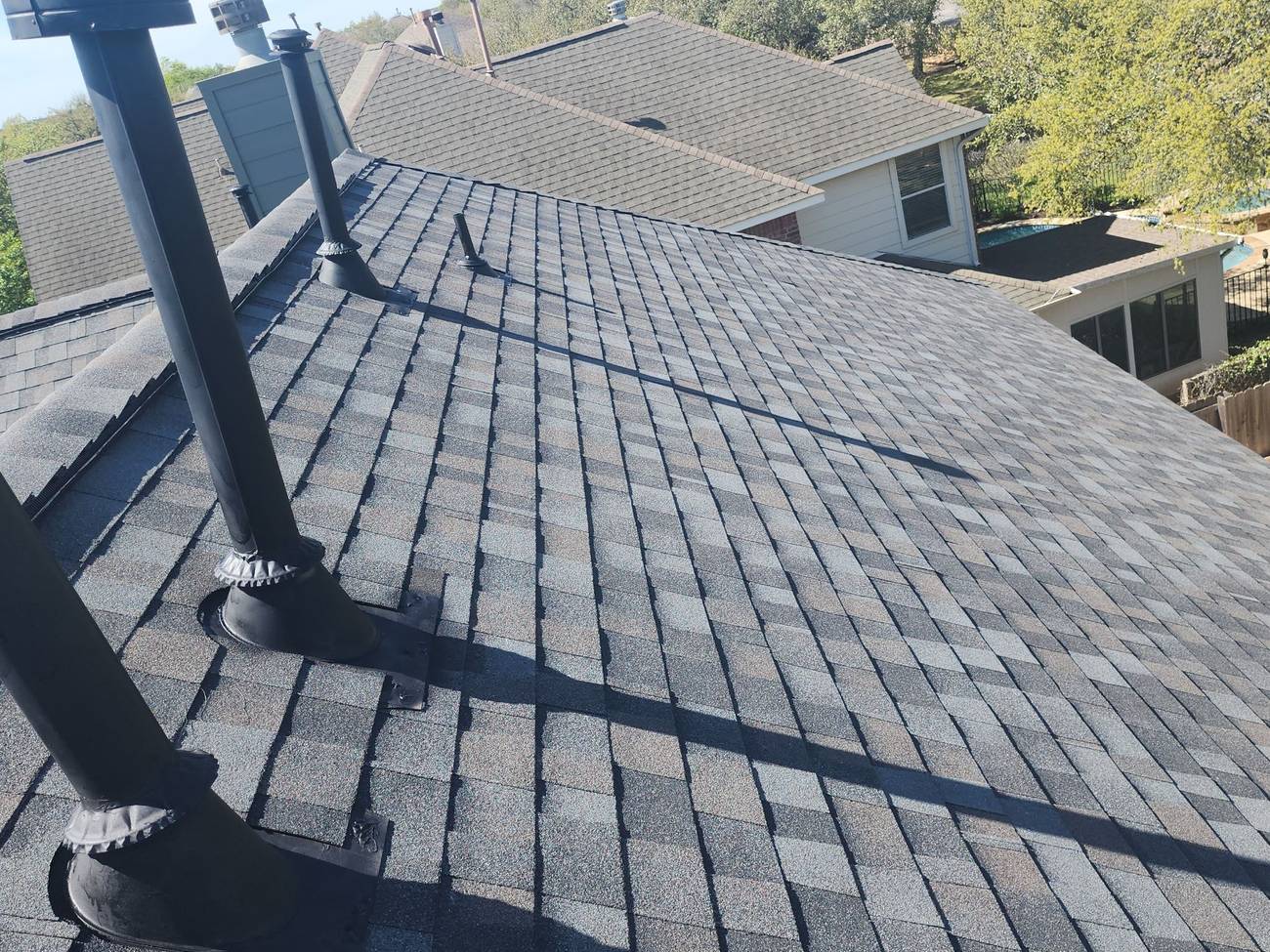 A charcoal architectural shingle roof with fresh pipe-boot flashings on each penetration
