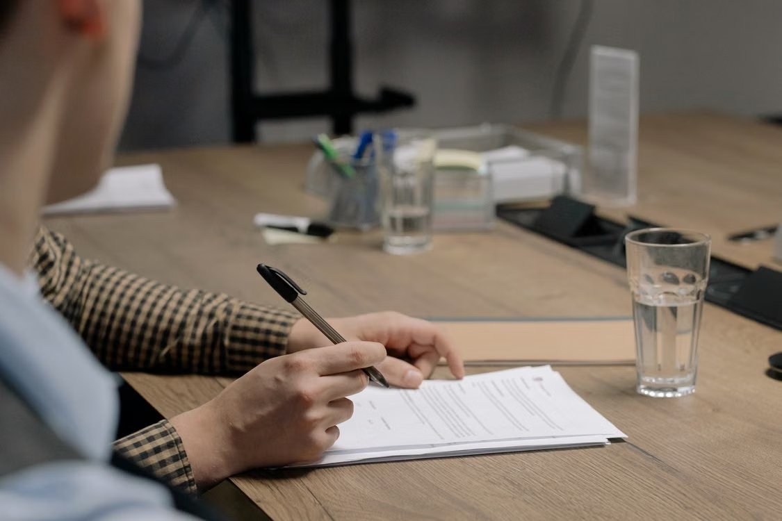 Person working on paperwork and holding a ballpoint pen in office setting.