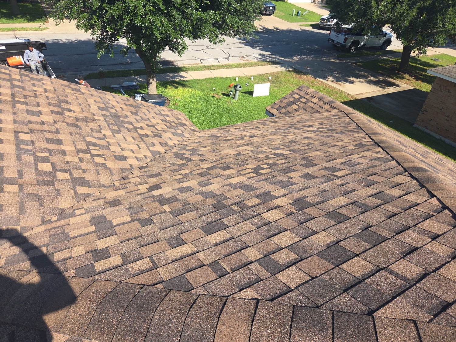 A freshly installed architectural shingle roof on an Austin home seen from the ridge, with the crew's truck at the curb