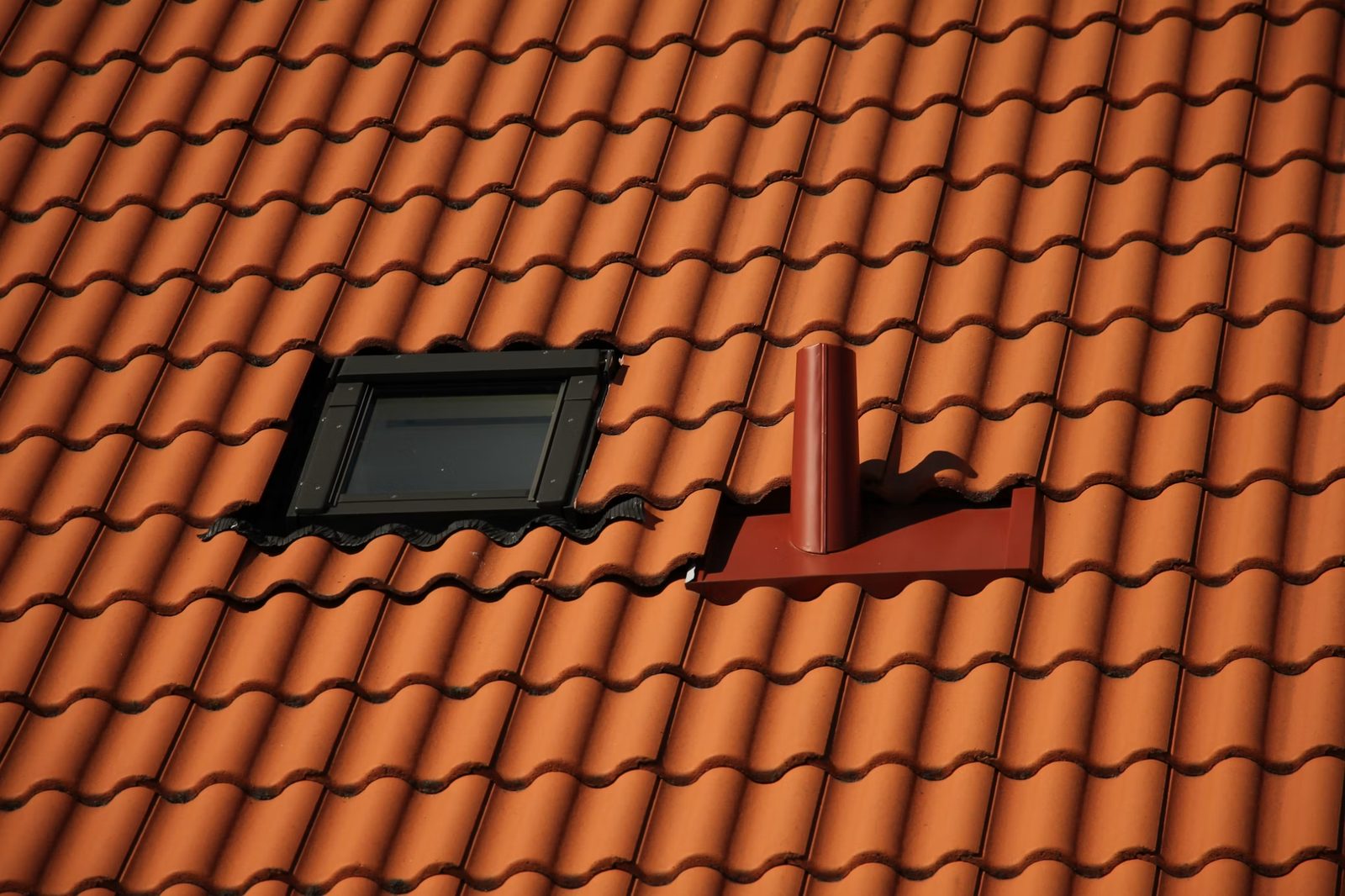 Roof chimney and flashing against window on an orange-tiled roof