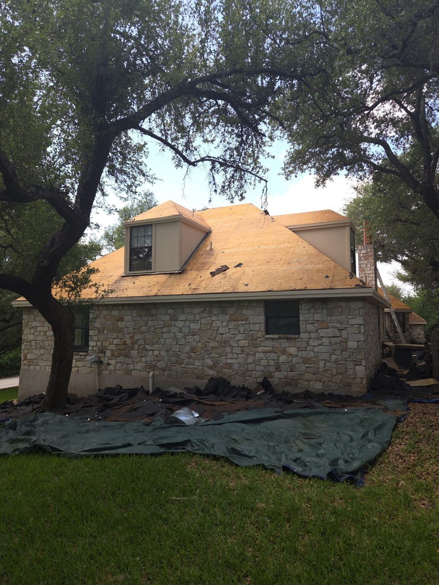 A stone-exterior Austin home during the roof decking replacement phase, showing exposed plywood and site protection