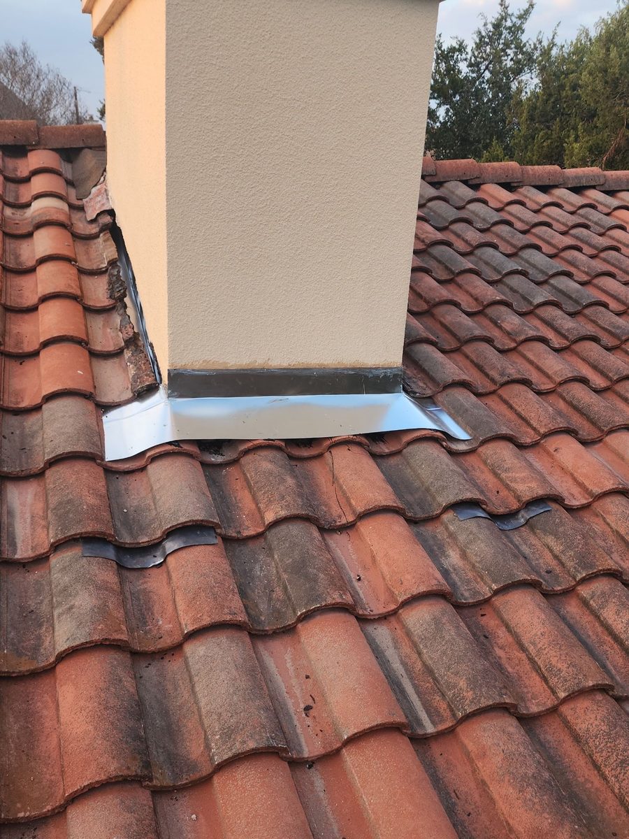 New metal flashing worked into a clay tile roof around a chimney
