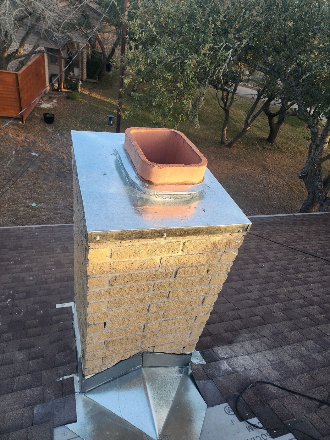 New galvanized chimney cap installed on the same chimney structure with the clay flue pot set into the cap base, freshly poured wash and counter-flashing returned.