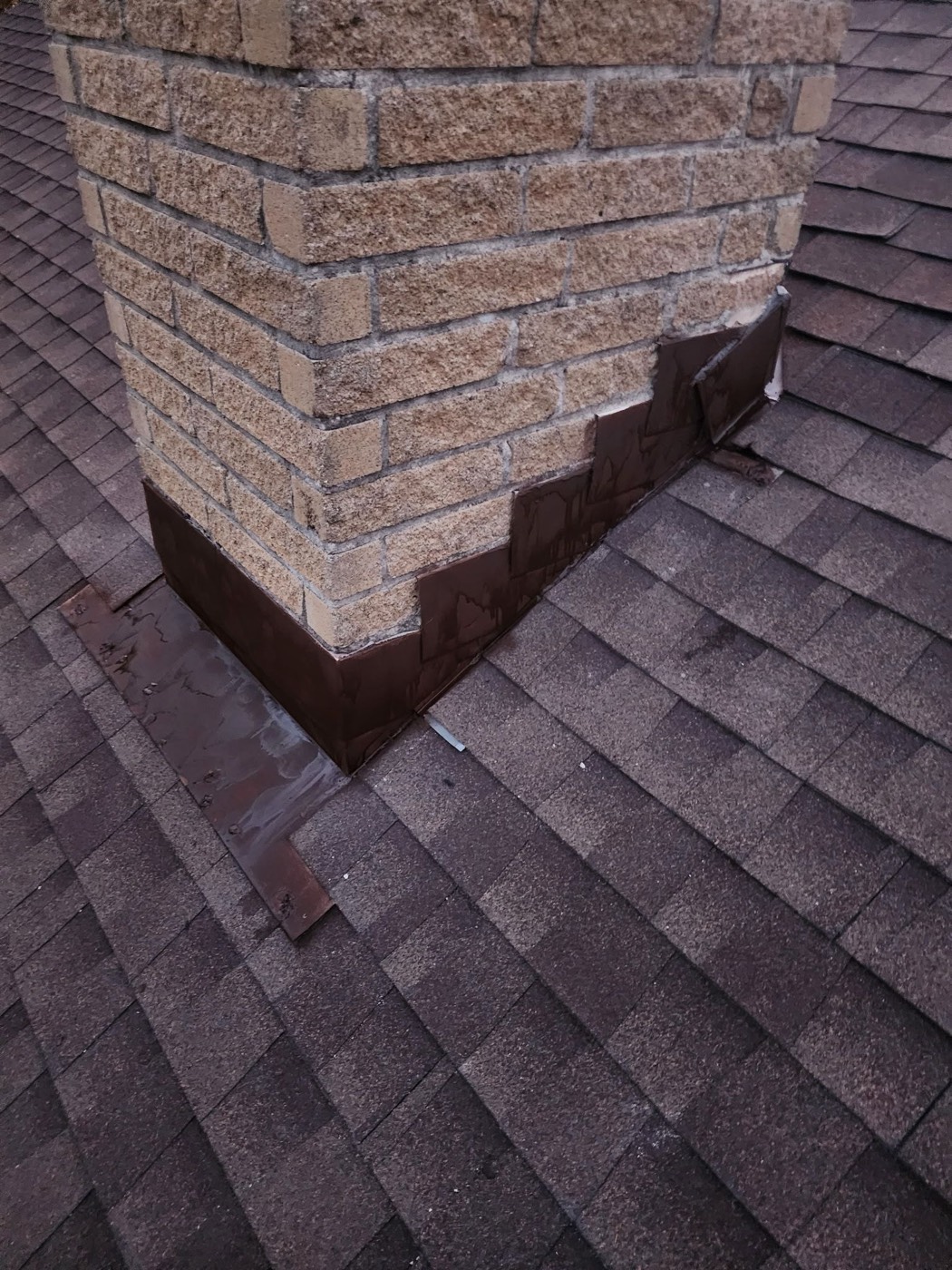 New step flashing installed at the chimney-to-roof intersection on the same Mr. Vasquez project, hand-folded brown and integrated into a fresh shingle field with a clean step lap.