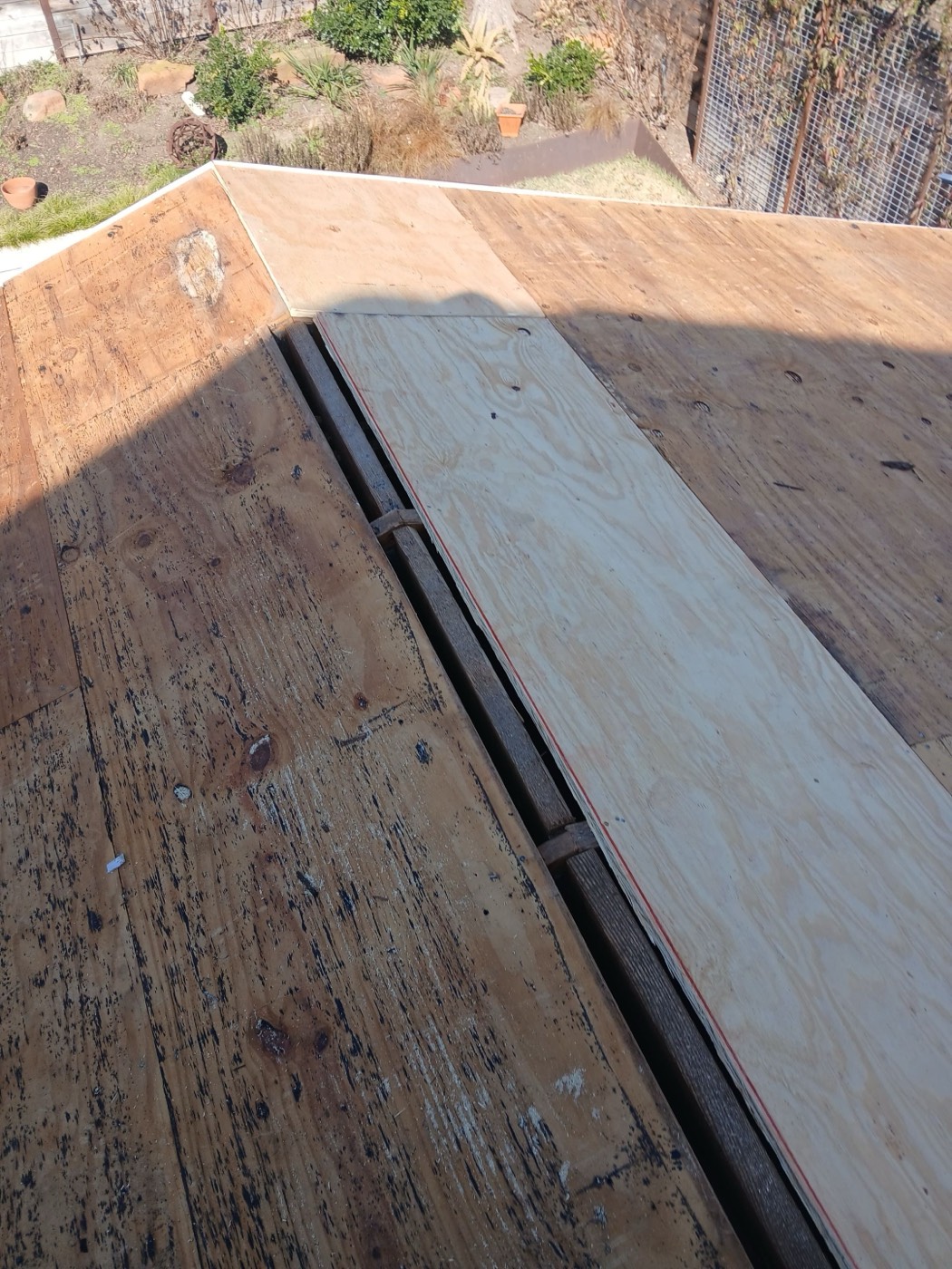 Fresh plywood patch laid over original decking with a red sealant line along the joint, photographed before underlayment goes down. Decking replacement filed and approved on the supplement.